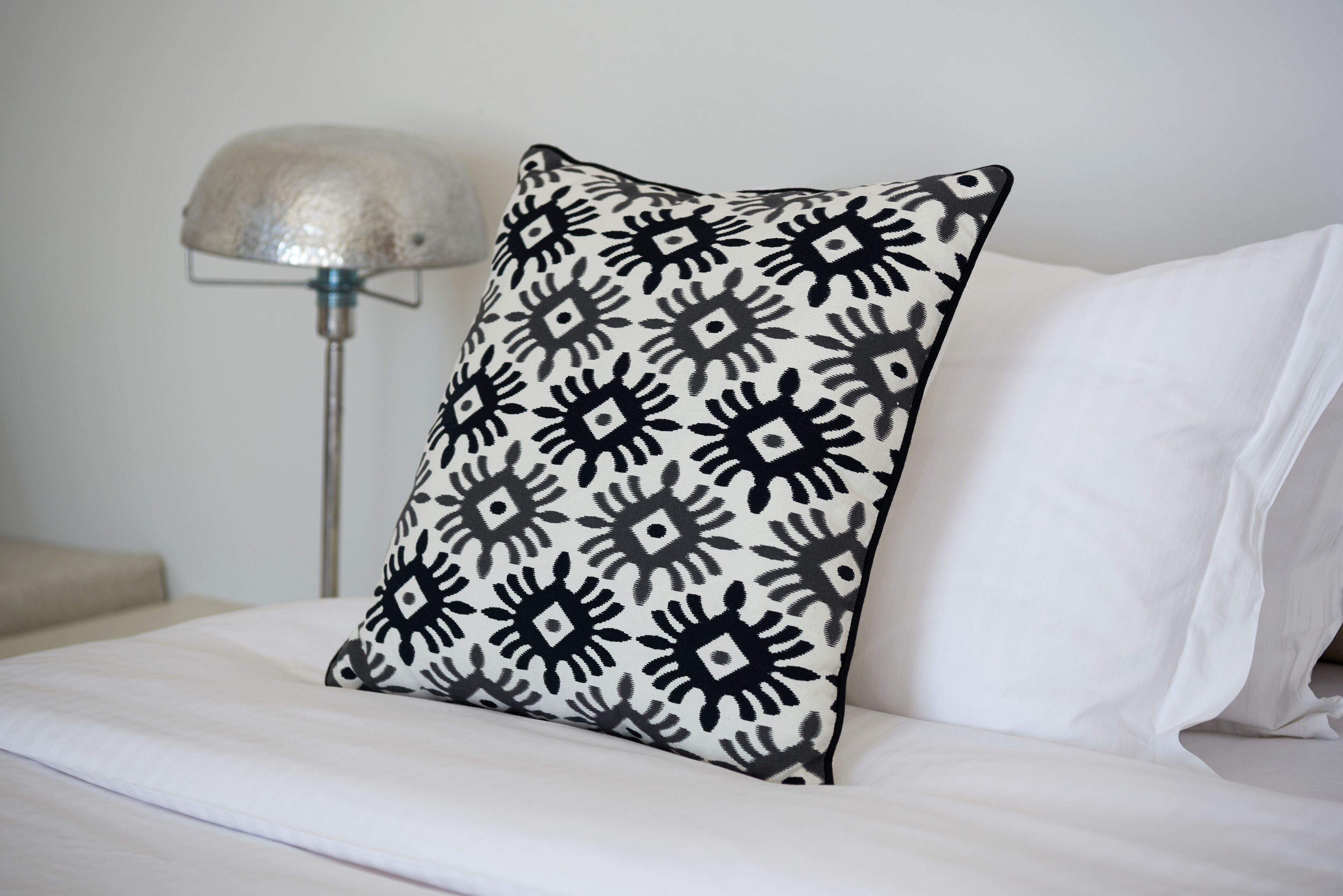 A bed with white bedding and a black and white patterned pillow.
