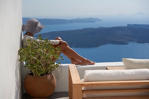 A person relaxing on a balcony with a view of the sea and hills. - Native Eco Villas (Santorini)