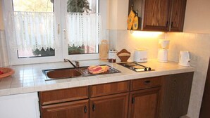 Une cuisine avec des meubles de rangement en bois, un évier, une machine à café et une fenêtre avec des rideaux.