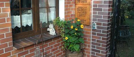 A brick building with a window, a wooden sign, and a potted plant with yellow flowers.
