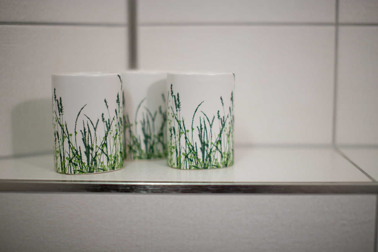 Due tazze di ceramica bianca con decorazioni a motivi erbosi su uno scaffale bianco.