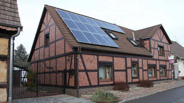 Une maison traditionnelle à colombages, dotée d’un toit en pente et de panneaux solaires.