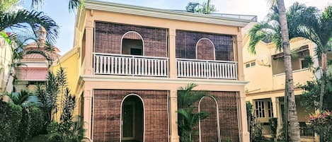 Un bâtiment à deux étages doté d’un balcon, entouré de verdure et de palmiers.