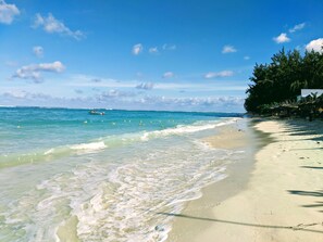 A beach with clear turquoise water, a sandy shore, and a few boats in the distance. - TOPHOME GOLD COAST (Flic-en-Flac)