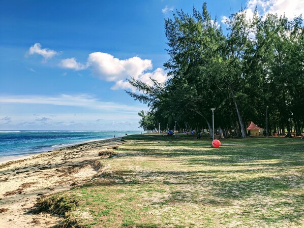 A beach with a grassy area, a red ball, and a small building in the background. - TOPHOME GOLD COAST (Flic-en-Flac)