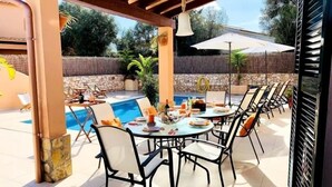 Een terras buiten met een zwembad, eettafels en stoelen.