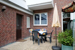 Eine Terrasse mit Tisch, Stühlen, einer Tür und einem Fenster.