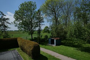 A rural landscape with a path leading to a small shed, surrounded by lush greenery and trees.