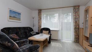 A living room with a sofa, armchair, table, and a television. - Vacation house Langeoog, Baumann - Vacation house Baumann (Esens)