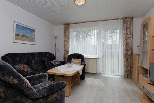 Ein Wohnzimmer mit Sofa, Sessel, Tisch und Fernseher.