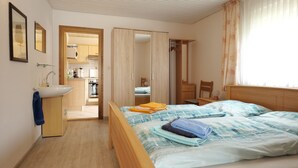 A bedroom with a bed, a bedside table, a wardrobe, and a bathroom with a sink. - Vacation house Langeoog, Baumann - Vacation house Baumann (Esens)