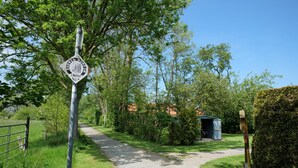 A rural pathway with a directional sign, surrounded by greenery and a small shed. - Vacation house Langeoog, Baumann - Vacation house Baumann (Esens)