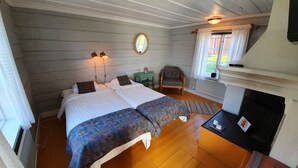A bedroom with a double bed, a chair, a small table, a mirror, and a window with curtains. - Lövångergården (Lövånger)