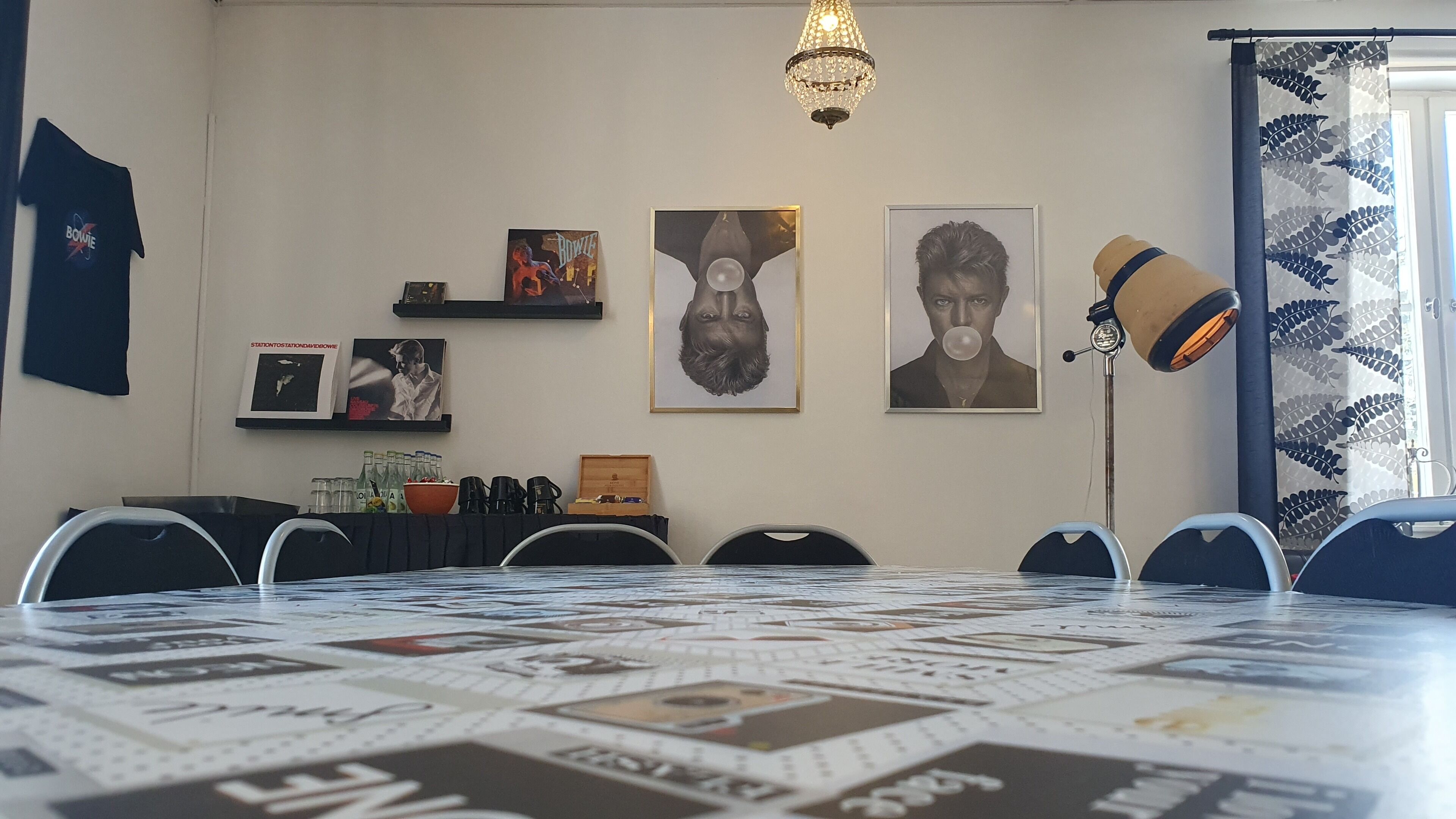 Un salón de conferencias con una larga mesa cubierta con un tablero de juego, rodeada de sillas. Hay cuadros enmarcados en la pared, una araña y una lámpara decorativa.