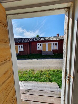 A view through a doorway of a building with a tiled roof, a wooden deck, and a grassy area with yellow flowers. - Lövångergården (Lövånger)