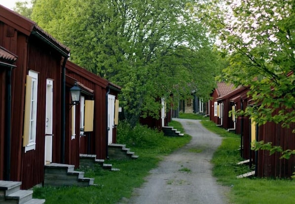 Une rangée de cabanes en bois, séparées par un étroit sentier, et entourées de verdure.