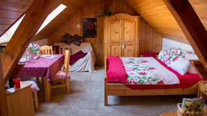 Un dormitorio acogedor en el ático, con techo de madera, una cama con ropa de cama floral, un armario de madera y una pequeña mesa con sillas.