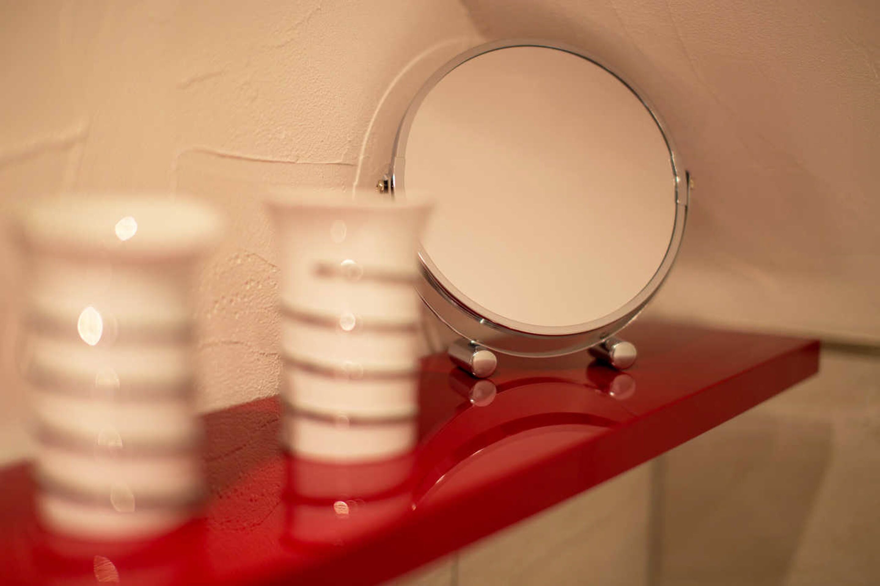 Un mobile bagno con uno specchio, uno scaffale rosso e un dispenser per sapone bianco.