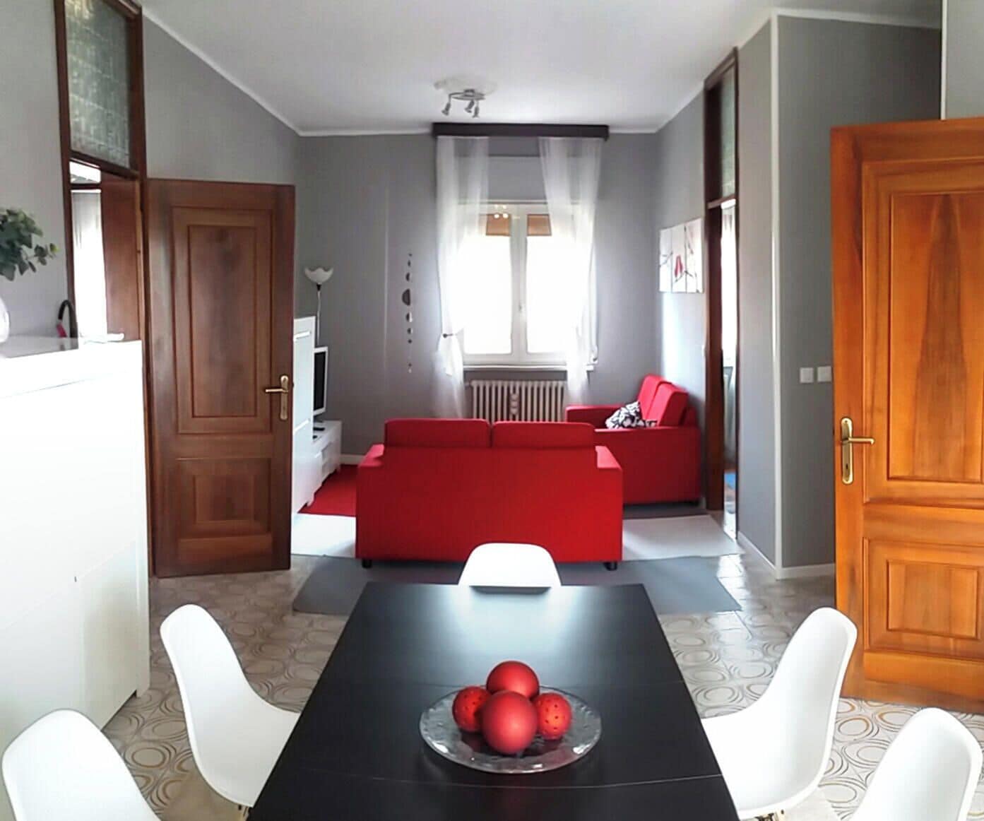 A living room with a red sofa, a dining table with white chairs, and a kitchen area with a white refrigerator.