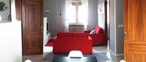 A living room with a red sofa, a dining table with white chairs, and a kitchen area with a white refrigerator.