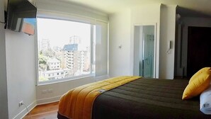 A bedroom with a large window, a bed with pillows, and a TV mounted on the wall. - Hotel Torreviña (Vina del Mar)