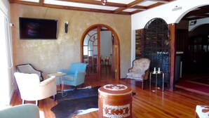 A spacious living room with wooden flooring, a large round ottoman, and a television mounted on the wall. - Hotel Torreviña (Vina del Mar)
