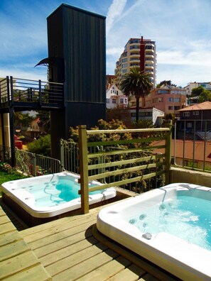 A rooftop with two hot tubs, a wooden deck, and a view of surrounding buildings.