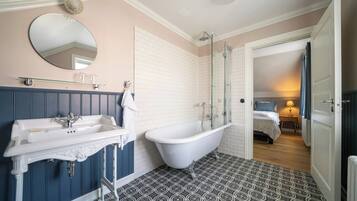 Un baño con bañera, lavamanos y espejo. Hay una puerta que da a un dormitorio.