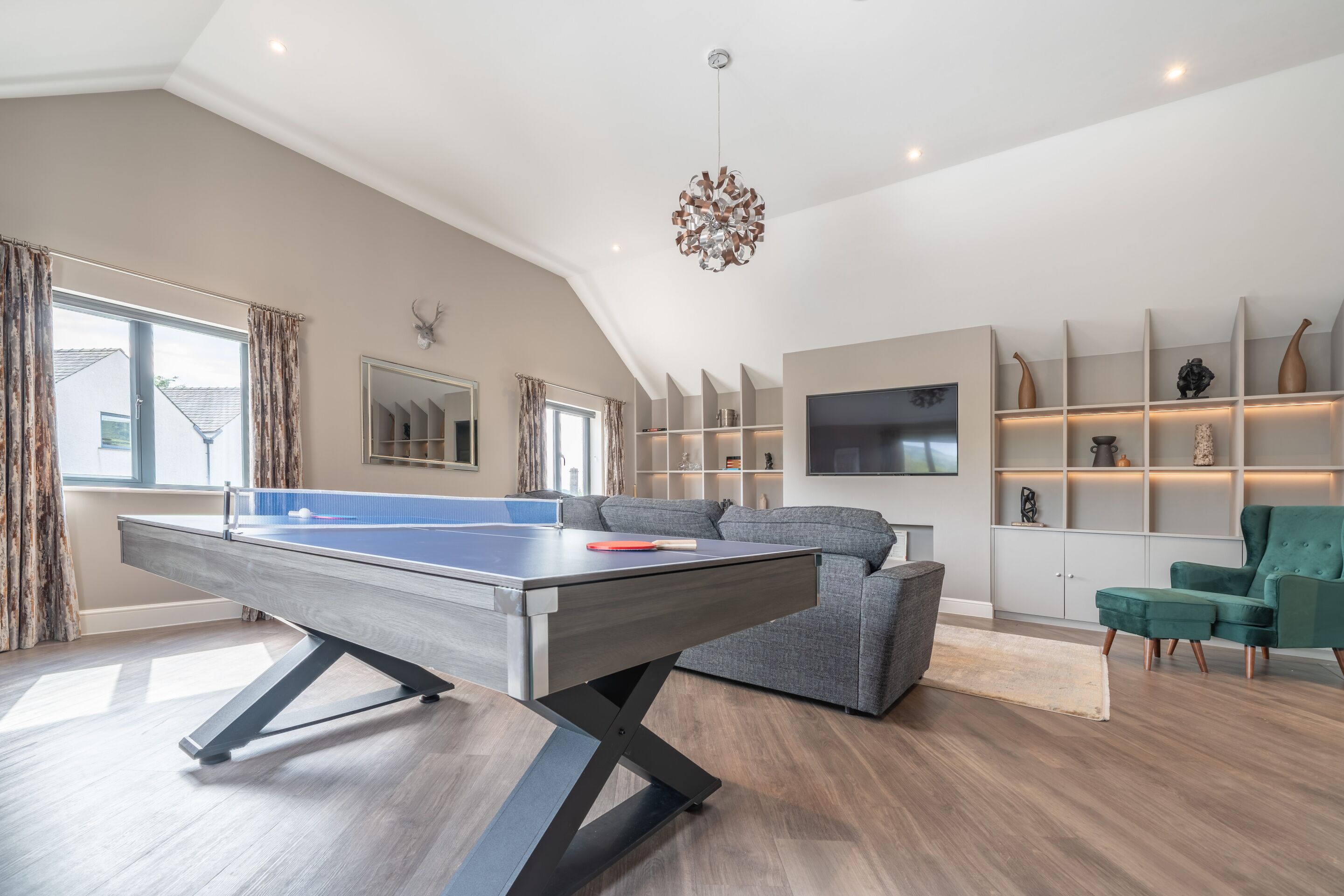 A modern living room with a ping pong table, grey sofa, and a TV.