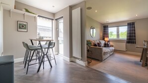A modern living room with a sofa, a coffee table, and a dining area with chairs. - The Penthouse @ Carus Green (Kendal)