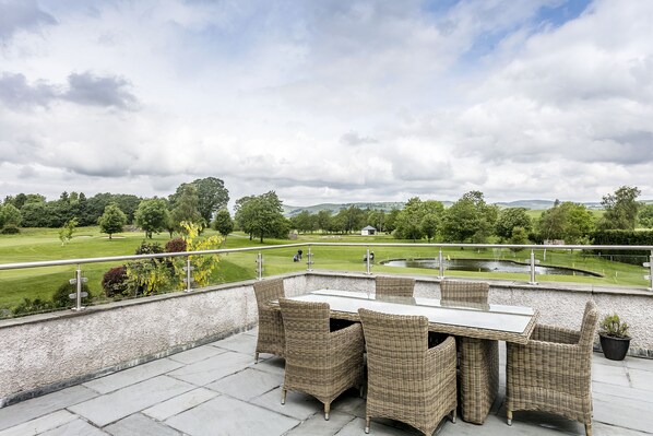 An outdoor patio with wicker furniture and a view of a golf course.