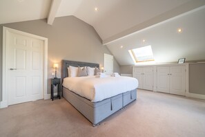 A bedroom with a large bed, a nightstand, a desk with a chair, and a skylight.