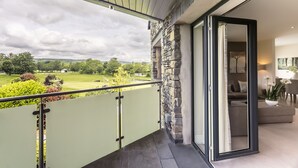 A balcony with a view of a green landscape, a stone wall, and a modern living room with a sofa and a table. - The Penthouse @ Carus Green (Kendal)