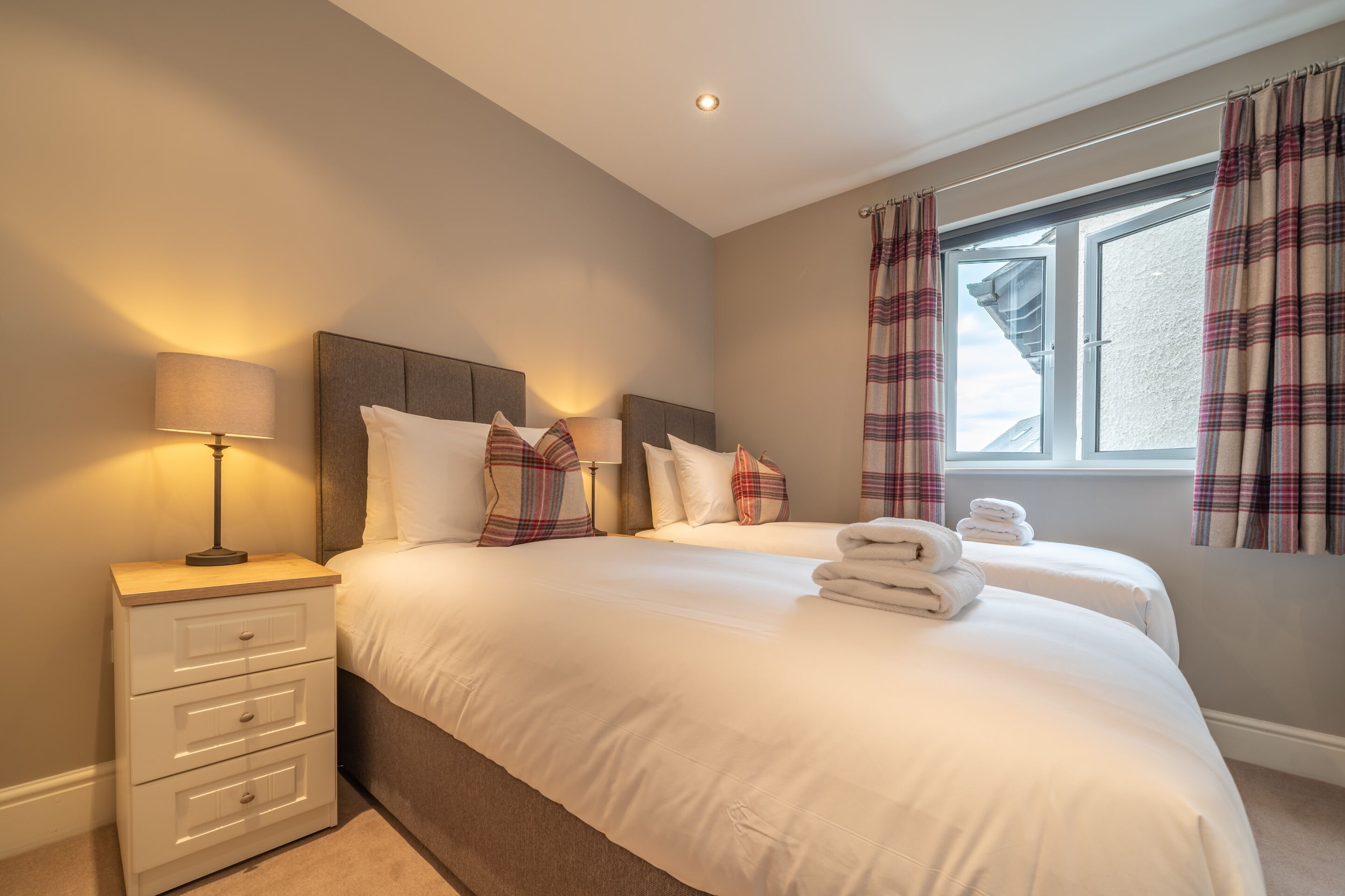 A hotel room with a bed, a nightstand, a lamp, and plaid curtains.