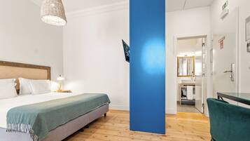 A hotel room with a bed, a desk, a chair, a blue pillar, and a hanging light fixture.