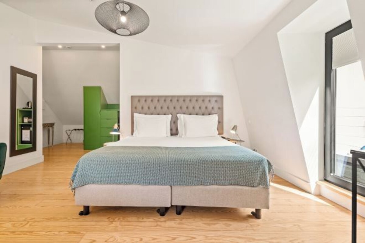 A modern bedroom with a large bed, a green accent wall, and a large window providing natural light.