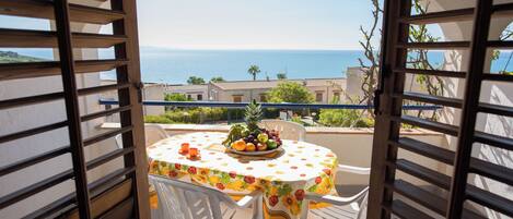 A balcony with a table set for two, overlooking a coastal view.