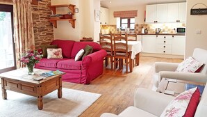 A cozy living room with a red sofa, a white armchair, and a wooden coffee table. A kitchen is visible in the background with white cabinets and a microwave. - A peaceful escape in rural Herefordshire - perfect for families and friends. (Nr. Hereford)