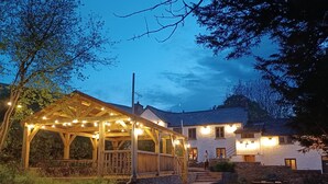 A wooden gazebo with string lights, a stone pathway, and a grassy lawn. - A peaceful escape in rural Herefordshire - perfect for families and friends. (Nr. Hereford)