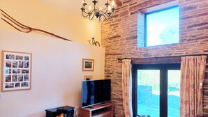 A cozy living room with a stone wall, a fireplace, a flat-screen TV, and a large window with curtains. - A peaceful escape in rural Herefordshire - perfect for families and friends. (Nr. Hereford)