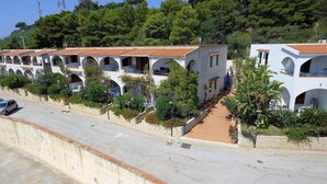 A row of white buildings with red-tiled roofs, surrounded by greenery and a paved road. - Holiday Home in Sciacca Mare Tennis Soccer Field, Barbecue, Wifi, Kitchenette (Valderice)