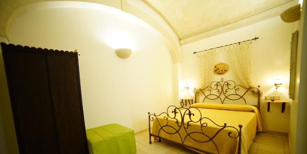 Una camera da letto con un letto, un poggiapiedi verde, una lampada a parete e una tenda.