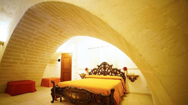 A bedroom with a vaulted ceiling, a wooden bed, a red bench, and a wooden door. - B&B Del Castelvecchio (Matera)