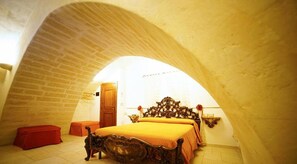 Un dormitorio con techo abovedado, una cama de madera, un banco rojo y una puerta de madera.
