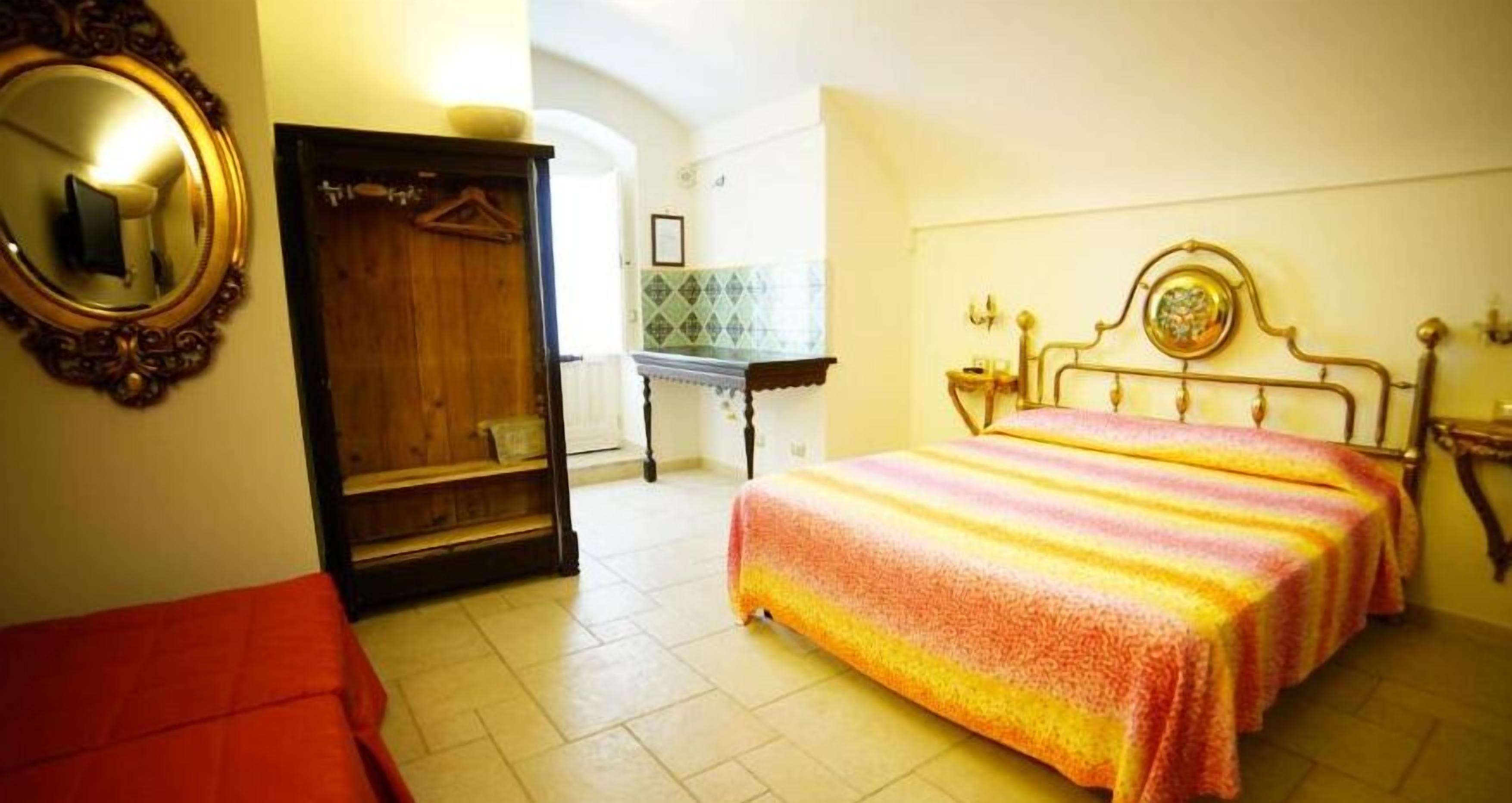 A bedroom with a bed, a wardrobe, a mirror, and a small table.