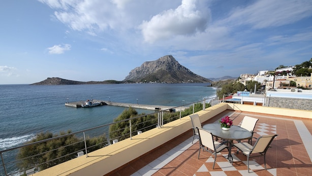 A terrace with a view of the sea, a rocky island, and a building with a sign.