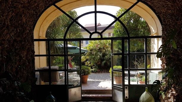 An arched doorway with a grid of glass panes leading to a garden area with potted plants and a bicycle. - Dimora Aganoor Relais & Gourmet Experience (Cava de' Tirreni)