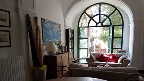 A cozy living room with a large arched window, a dining table with a bowl, and a sofa with a red blanket. - Dimora Aganoor Relais & Gourmet Experience (Cava de' Tirreni)