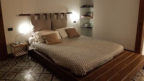 A bedroom with a bed, a nightstand, a reading lamp, a shelf with books and items, and patterned floor tiles. - Dimora Aganoor Relais & Gourmet Experience (Cava de' Tirreni)