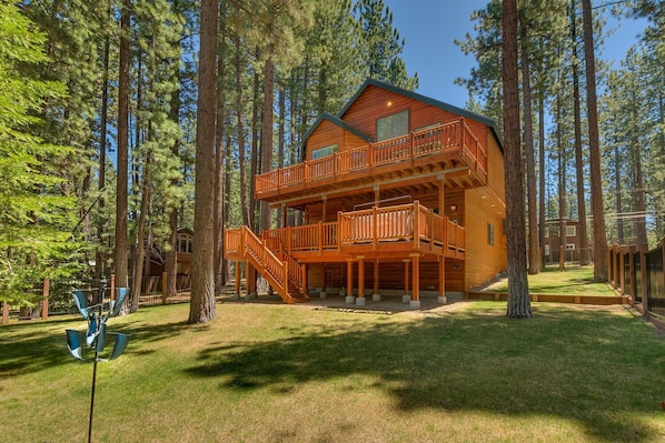 A two-story log cabin with a balcony, surrounded by tall pine trees.